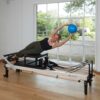 Pilates instructor using frame sitting box on Pilates reformer with exer-soft ball